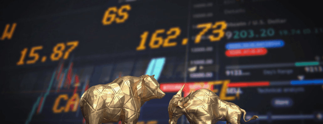 Gold bear figurine next to a gold bull figurine on a background with stock prices and data.