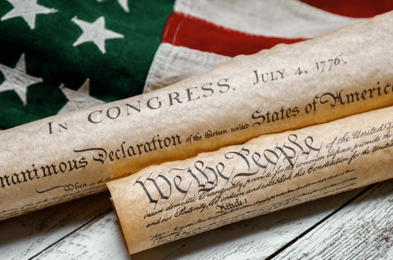 The Declaration of Independence and Constitution of the US rolled up and laying on an American flag.