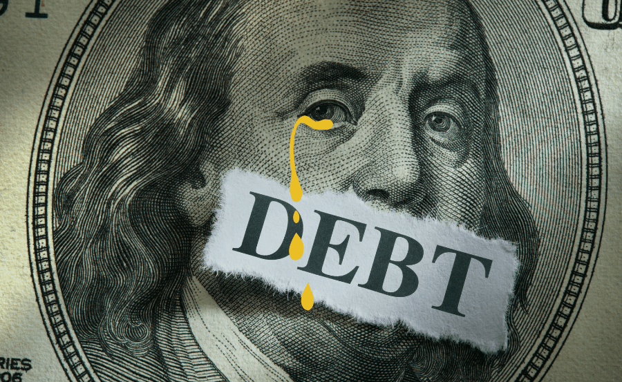 Closeup of Benjamin Franklin on the $100 bill, with a torn piece of paper featuring the word "debt" over his mouth and gold-colored tears falling from his right eye.